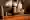 Cocktailglas mit orangefarbenem Drink, garniert mit einem Minzblättern welches vor dem Barkeeper steht. Dieser trägt ein weißes Hemd, eine schwarze Schürze und Fliege