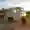 A beige-brown Piaggio Ape stands on a path between vineyards at sunset.