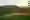 Grüne Hügel mit Weinbergen und kleinem Dorf im Tal bei Sonnenuntergang.
